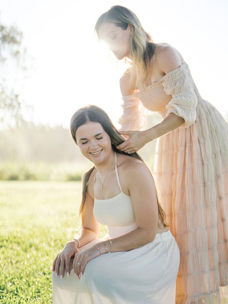 Young Woman Gently Styling Another Woman's Hair In A Golden Field, Photographed By A Gainesville Photographer Near Gainesville, Va
