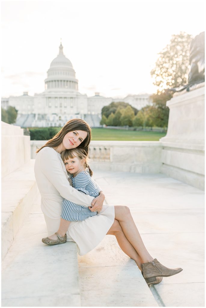 Mama and daughter sitting together, hugging, in front of the US Capitol building in DC