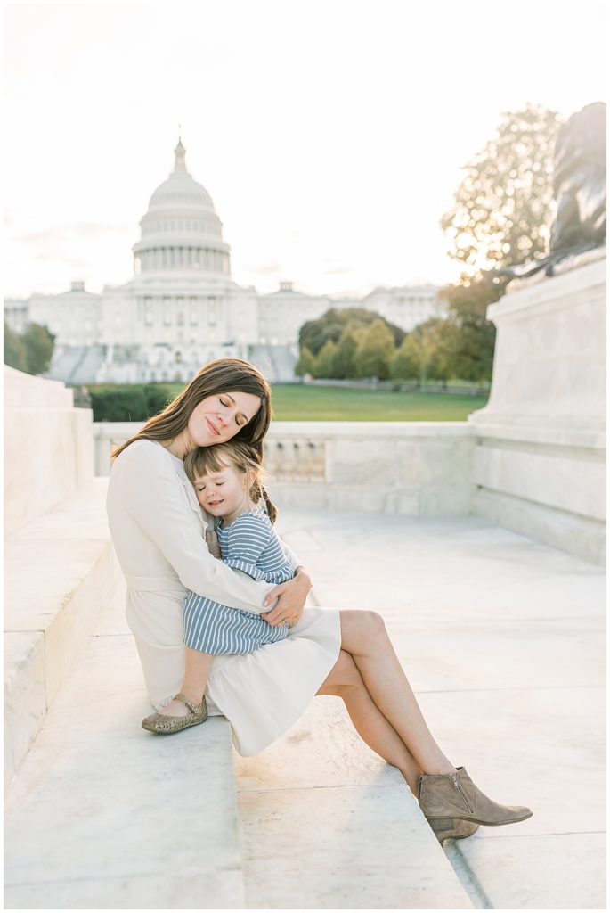 A mother holds her child, both closing their eyes, in front of the US Capitol.