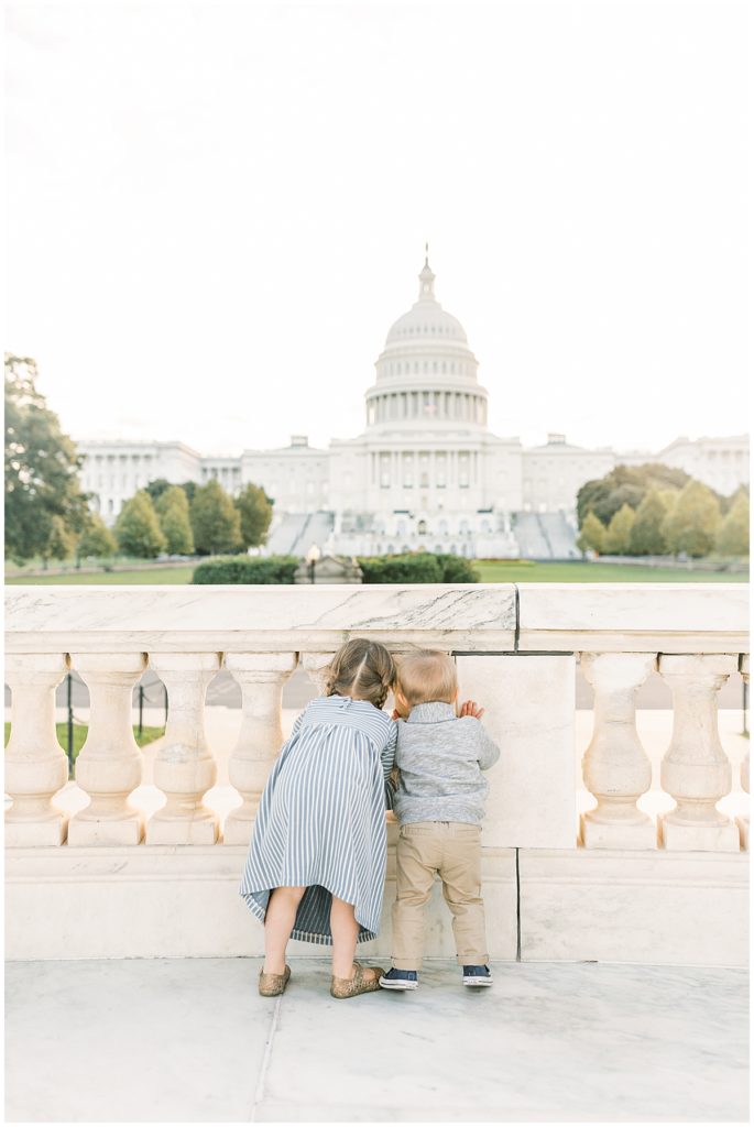 A young girl and boy looking through a railing at the US Capitol.