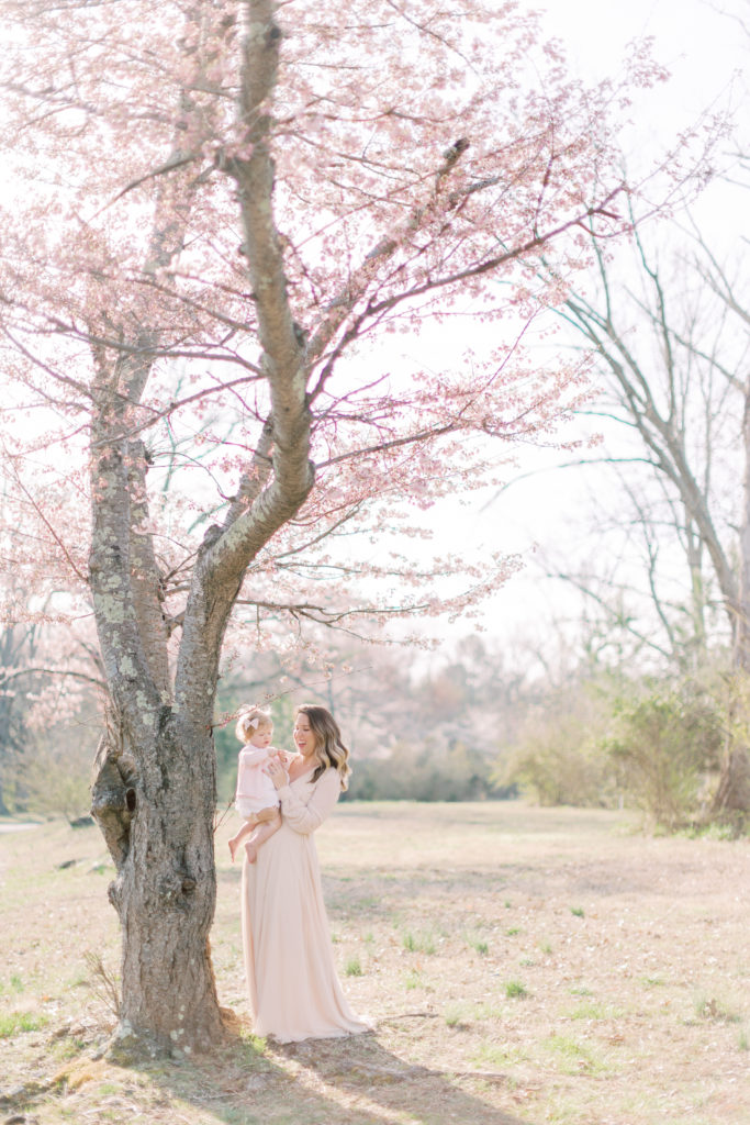 A mother holds her toddler daughter next to a cherry blossom tree in Maryland.
