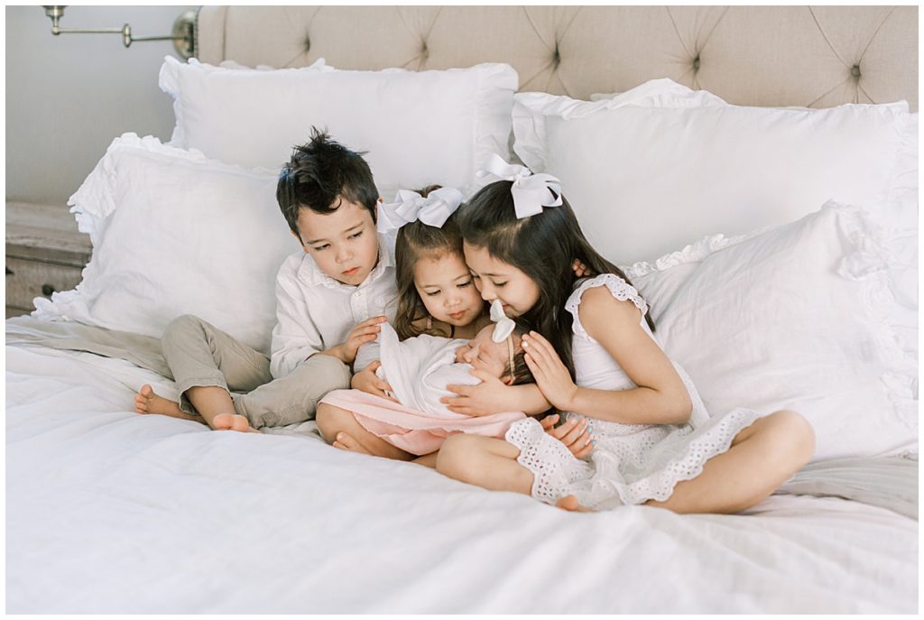 Children hold newborn baby on bed