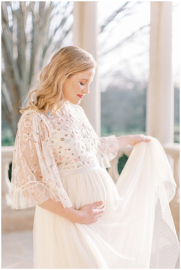 Pregnant woman holds up dress during maternity session at The Great Marsh Estate in Northern Virginia