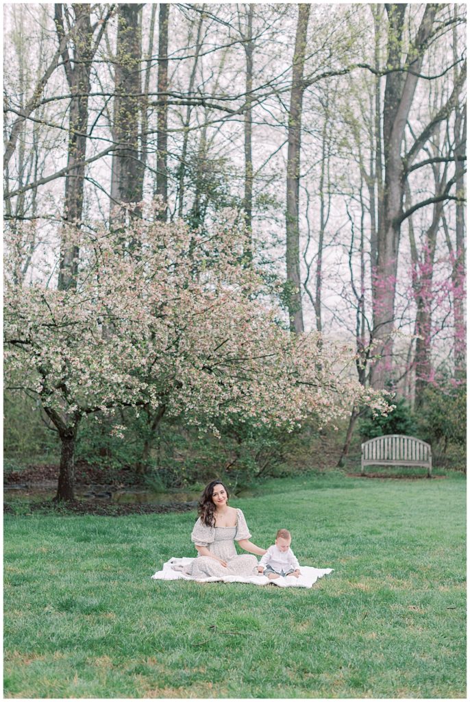 Mother sits with her baby next to the cherry blossom tree in Brookside Gardens