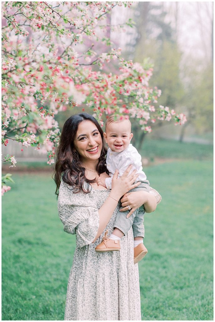 Mother holds her son by a cherry blossom in Brookside Gardens during Maryland family photo shoot.