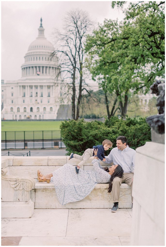 Family Photographers in DC | Mom lays down and holds son up in the air in front of the Capitol Building in DC