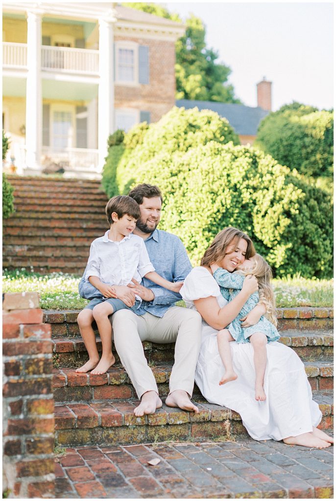 Family sits on steps while little girl hugs her mother during their Maryland photo session