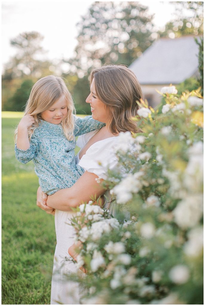 Mother holds her daughter near white floral bush at Mulberry Fields