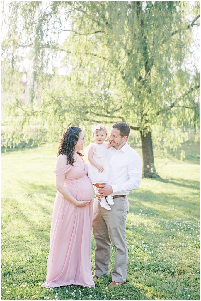 Mother and father stand with their toddler daughter during their Maryland maternity session