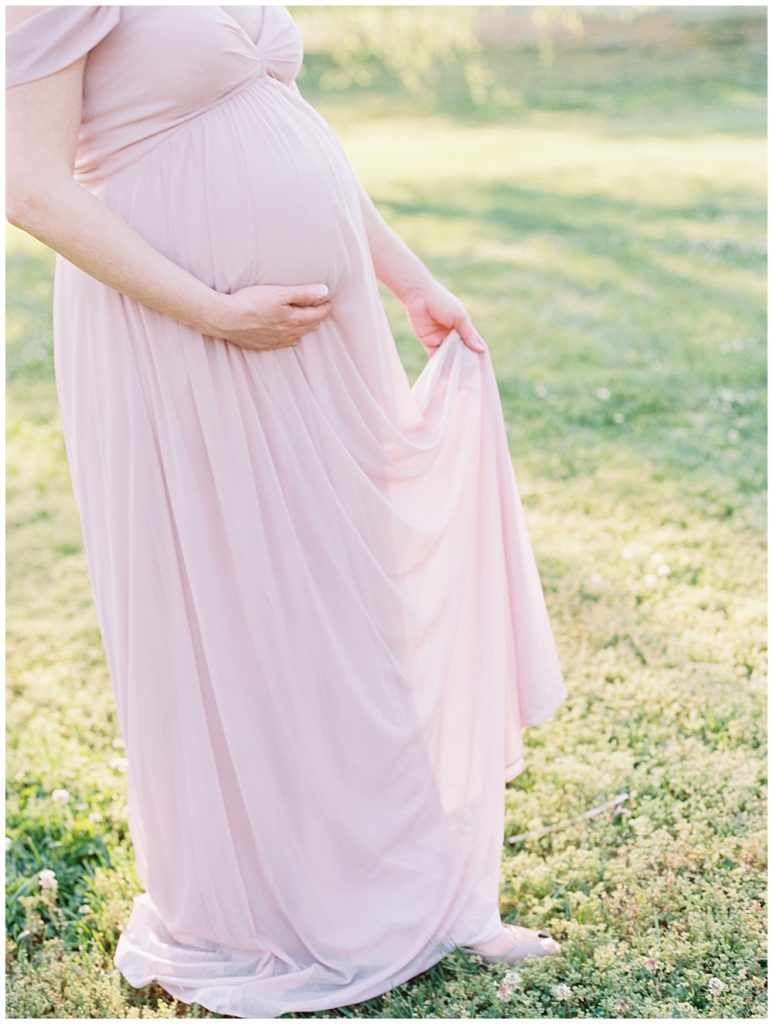 Pregnant woman stands holding her pink dress during maternity session