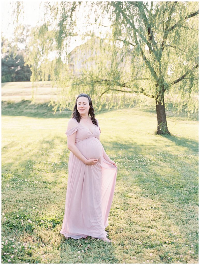 Pregnant woman stands in a field holding her pink dress