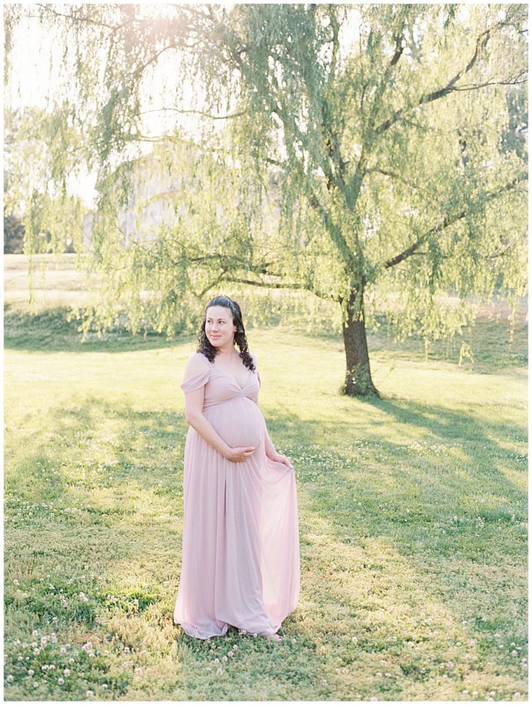 Woman stands near a willow tree during her Maryland maternity session