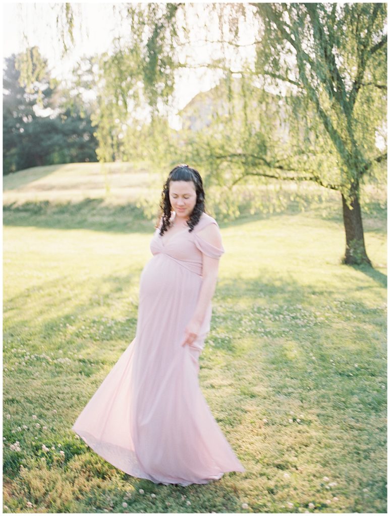 Pregnant woman twirls her dress in a grass field during her Maryland maternity session