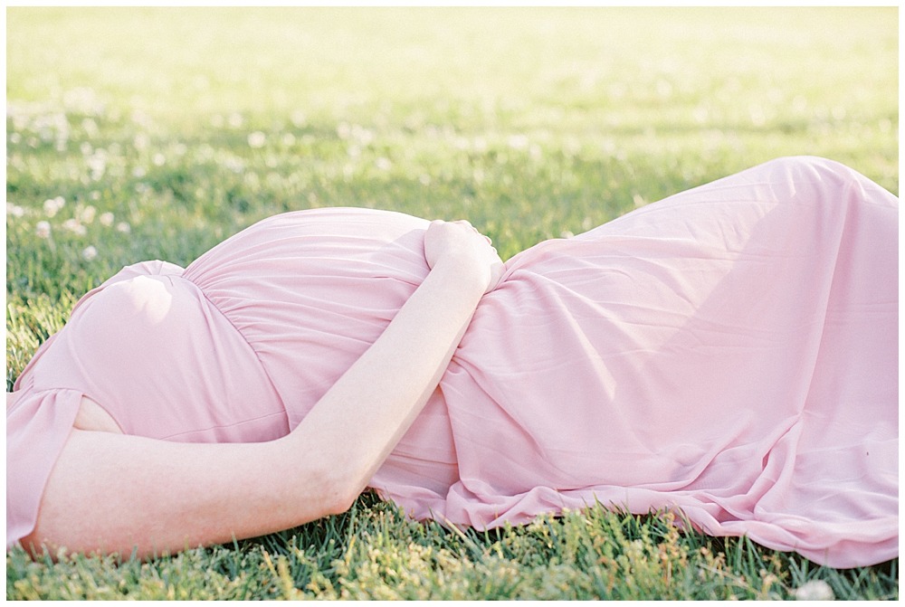 Woman lays down in a field during her maternity session