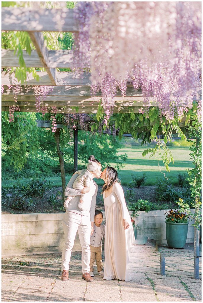 Mother and father kiss under the wisteria at Brookside Gardens in Silver Spring