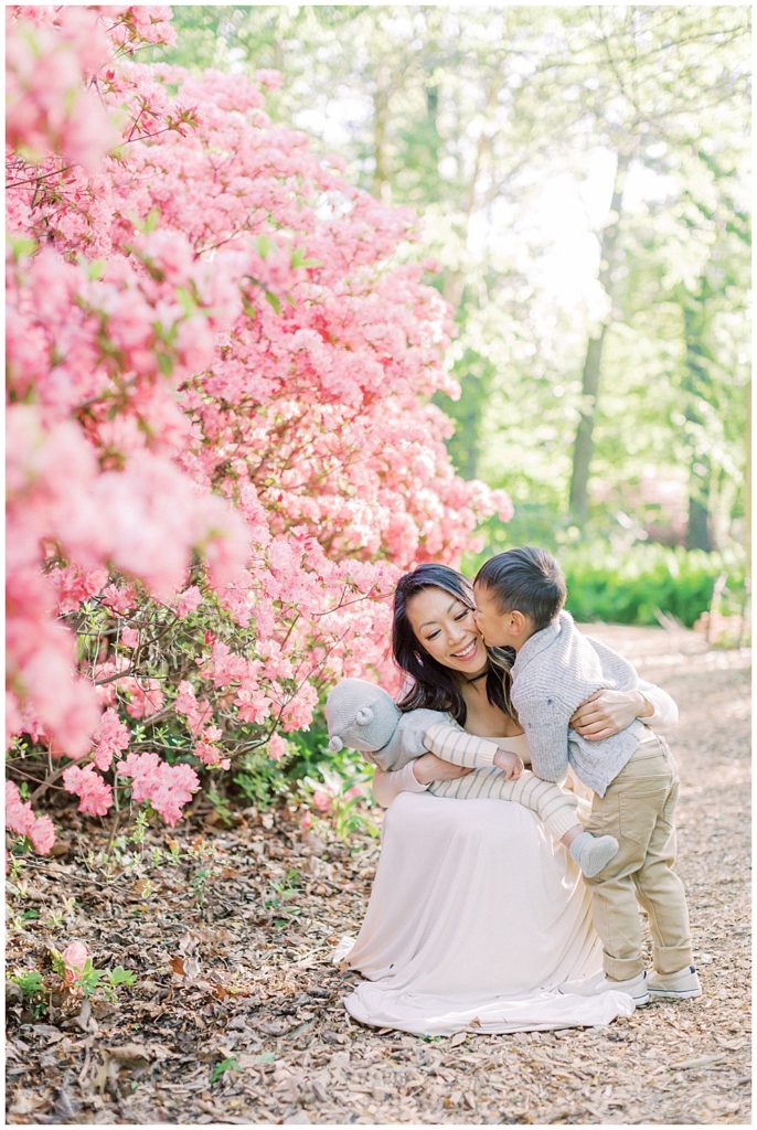 Little boy leans over and kisses his mother at Brookside Gardens by the pink azaleas