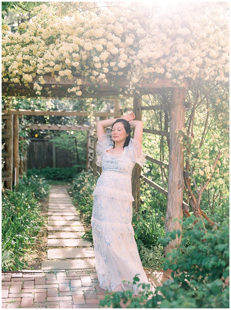 Best DC Photoshoot Locations |Pregnant woman stands with her hands behind her head near floral arch at Tudor House in DC