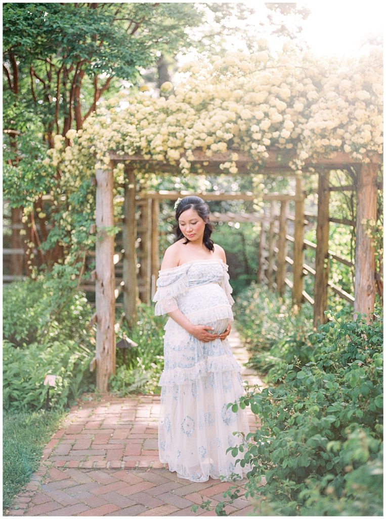 Pregnant woman stands near floral arch at Tudor Place during a DC maternity session