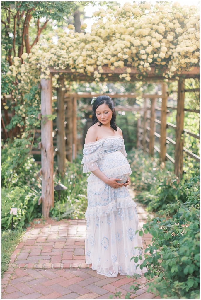 Pregnant mother stands with hands below her belly in Tudor House during maternity shoot