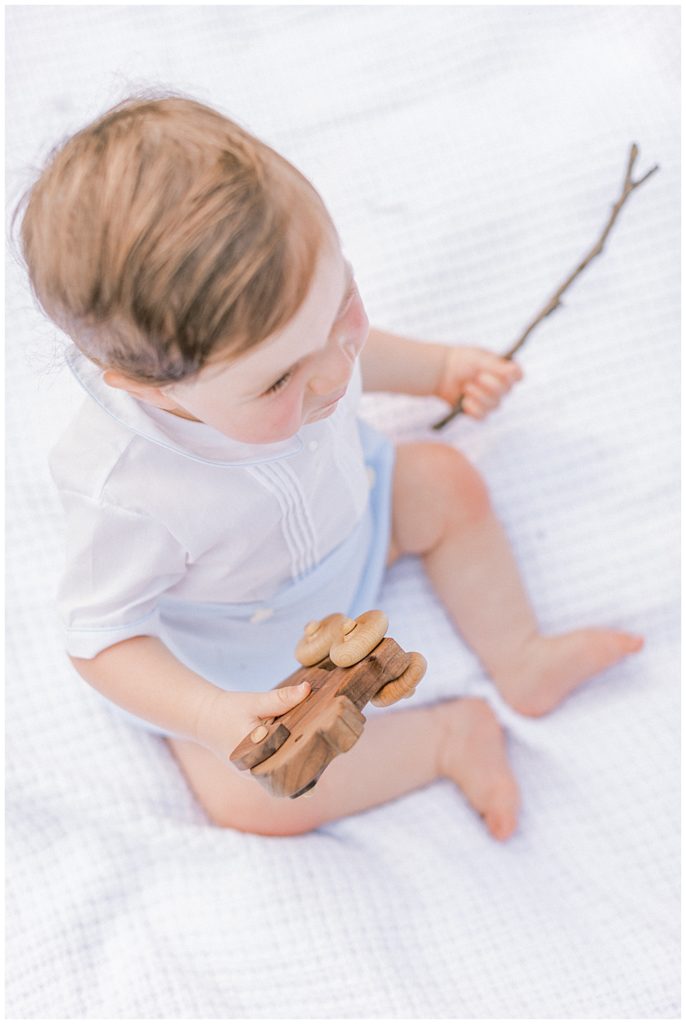 Overhead view of a one year old boy playing with a wooden train and a stick