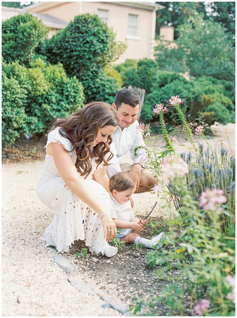 Mother and father kneel down to look at flowers with their one year old boy