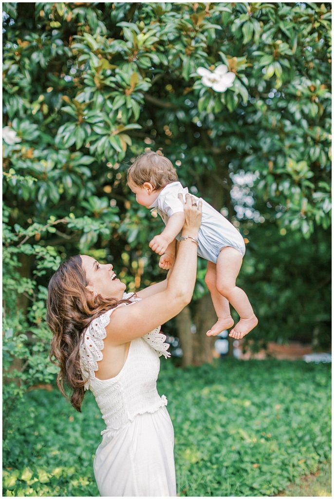 Mother holds up her son in the air in front of a large magnolia tree