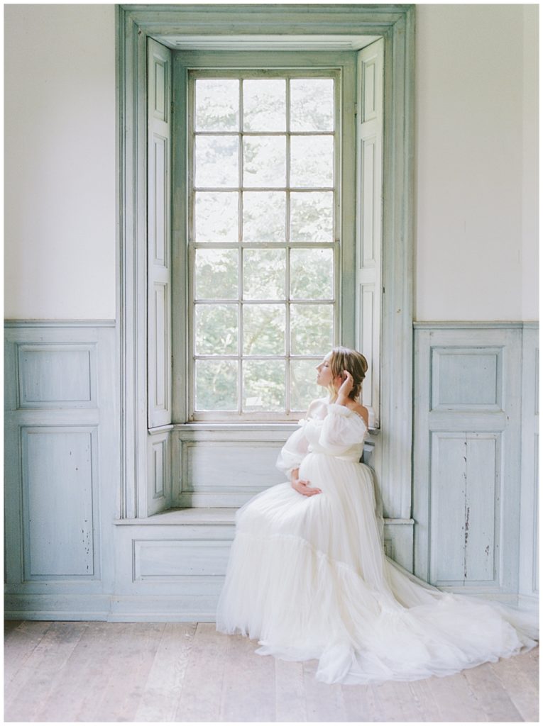 DC Maternity Photographer | Pregnant woman sits in a window during her NOVA maternity session at Salubria