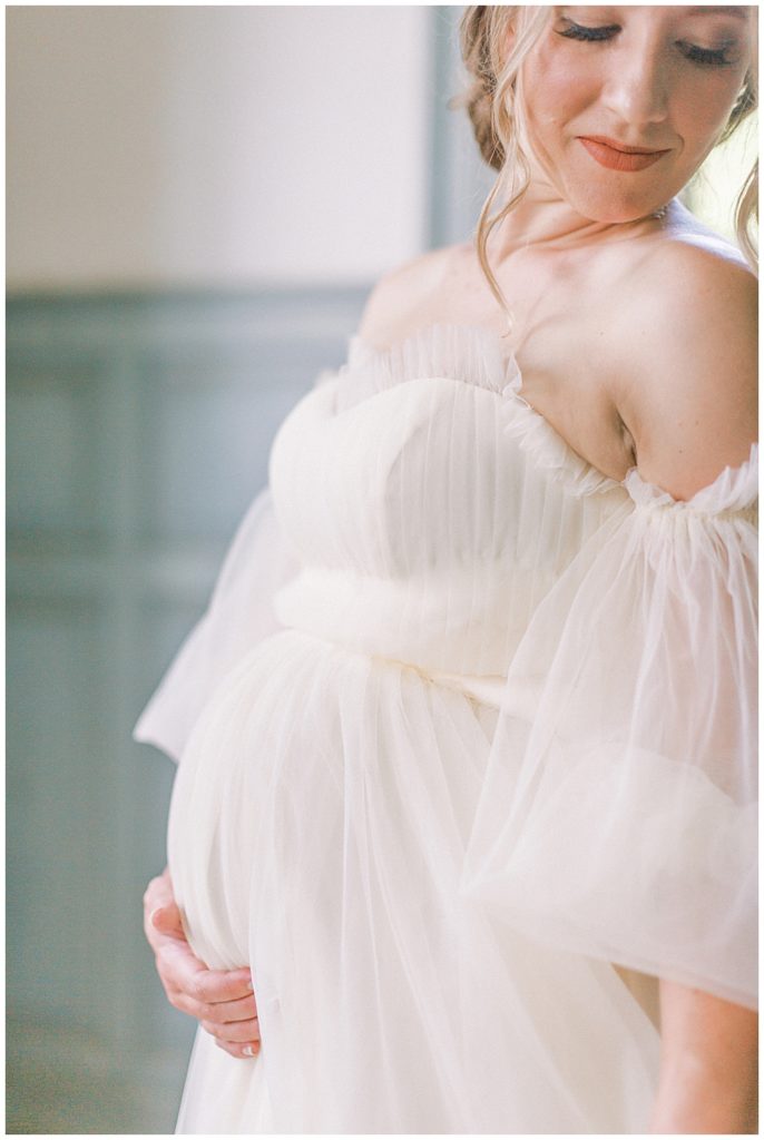 Pregnant woman in a white gown holds her belly
