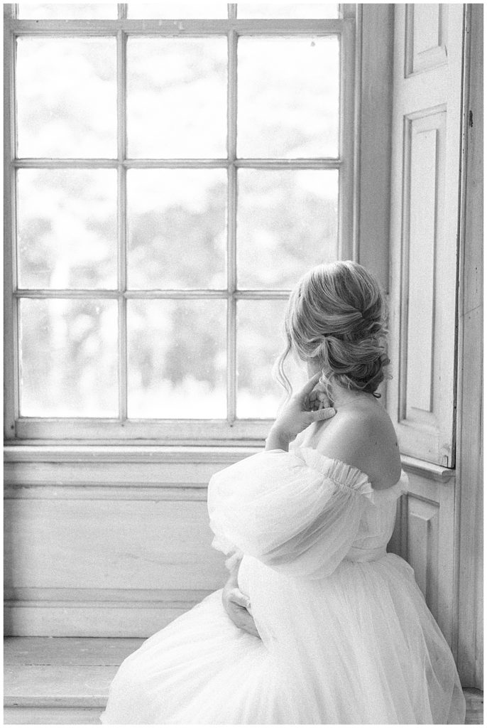 Black and white image of pregnant woman sitting in a large window