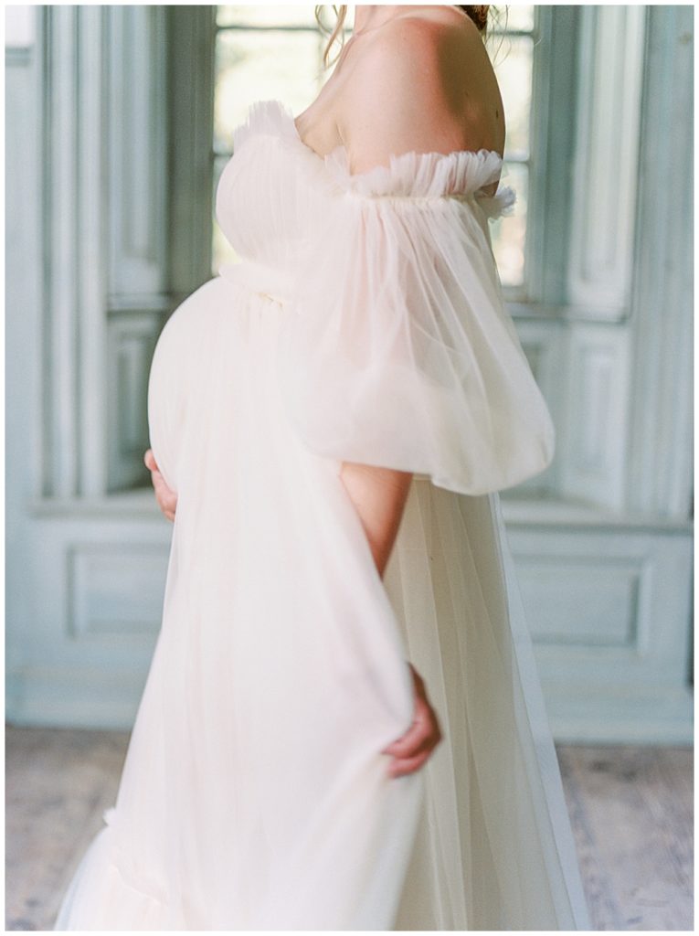 A woman stands, cradling her pregnant belly while moving her dress | Washington DC Maternity Photographer