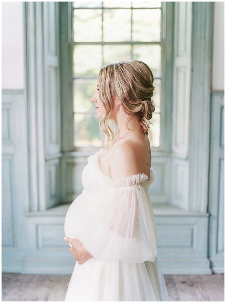 Woman stands with her hands below her belly in Salubria during her DC maternity session