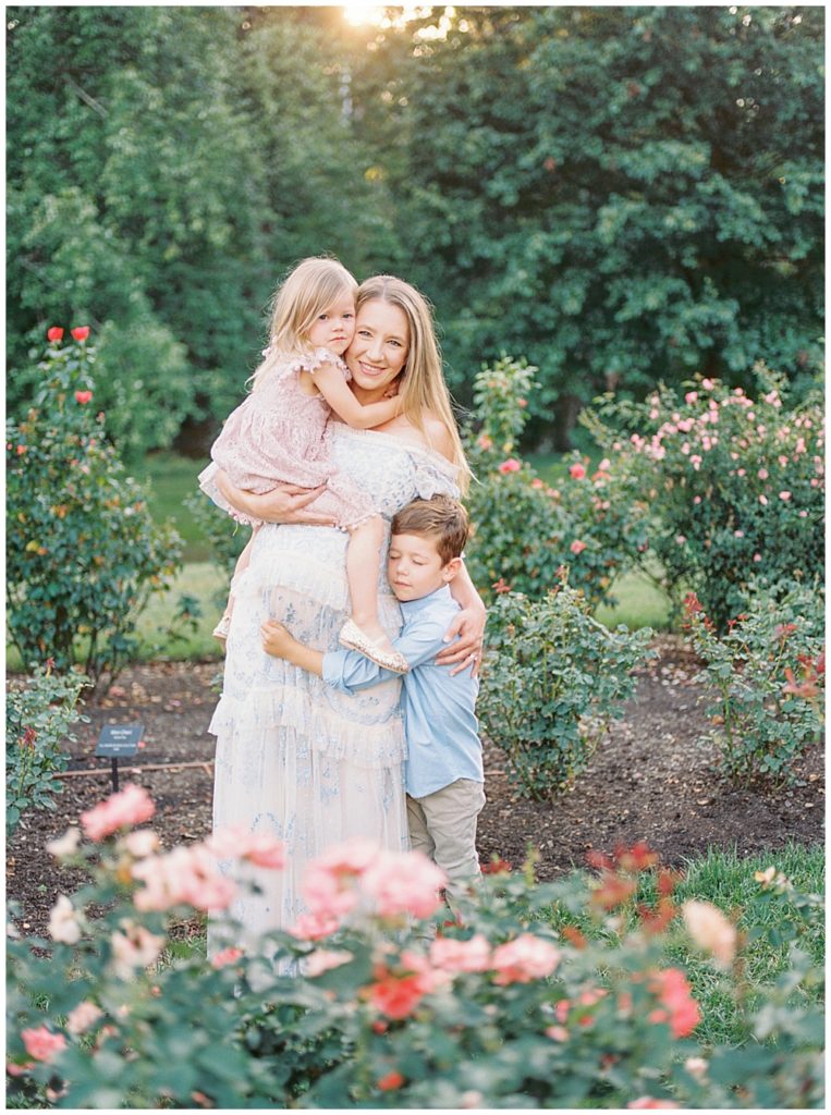 Little boy and girl hug their pregnant mother in the Bon Air Rose Garden in Arlington VA