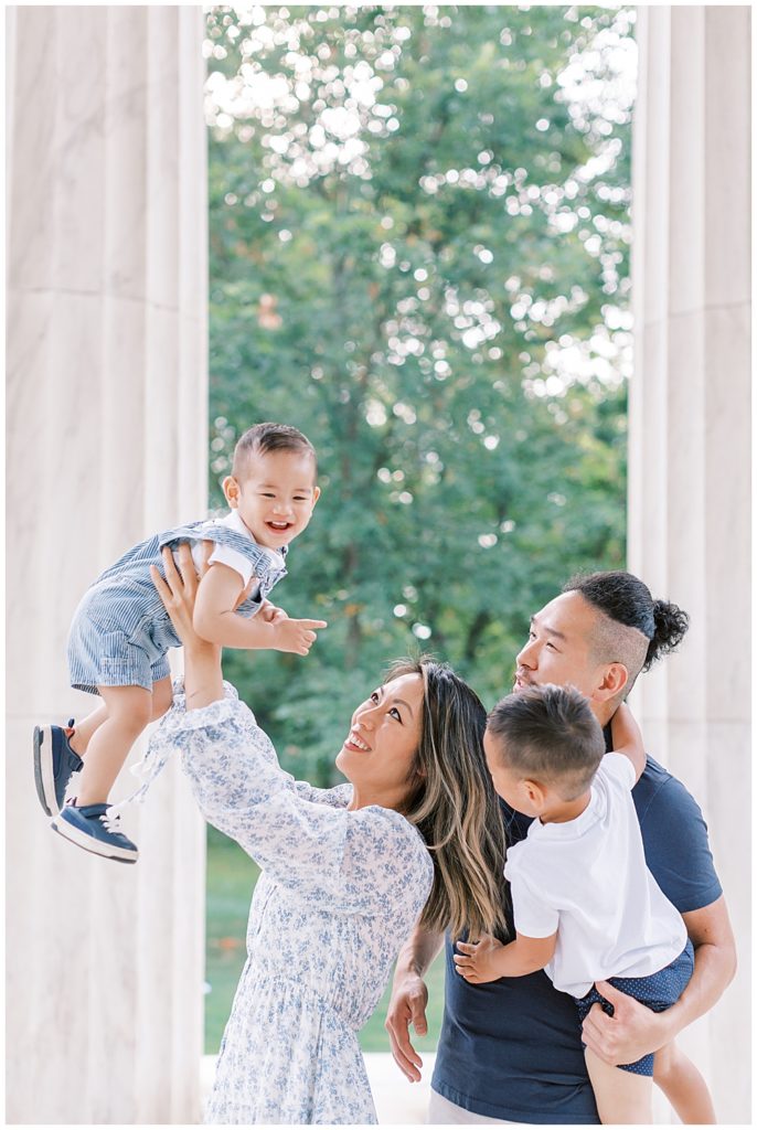 Mother holds son up into the air during their family photo session at the DC War Memorial in DC