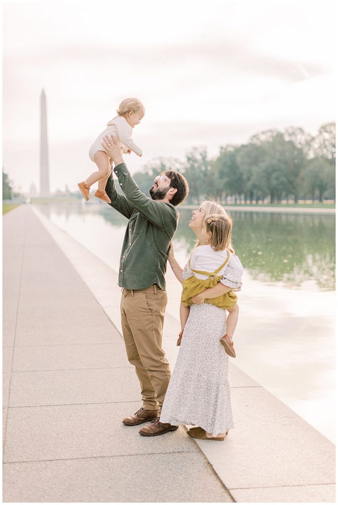 Family stands by the Reflecting Pool and holds up young daughter