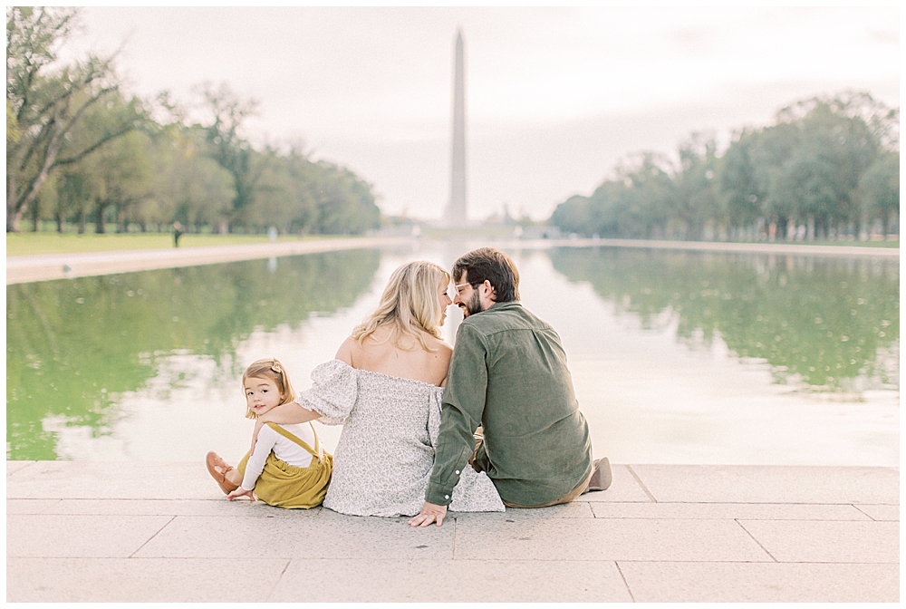 Family sits in front of the reflecting pool in DC facing the Washington Monument