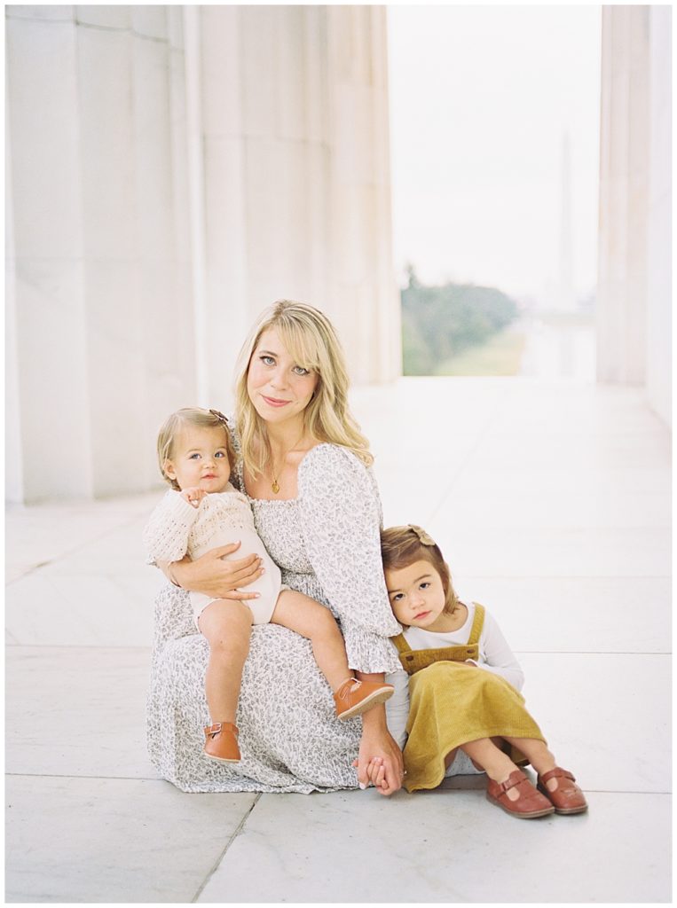 Mother sits with her two young girls at the Lincoln Memorial during her Washington DC family photo session