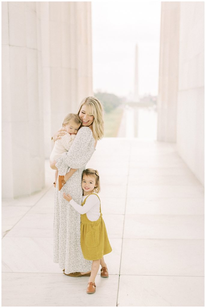 Mother stands holding one daughter while the other tugs at her dress at the Lincoln Memorial in DC