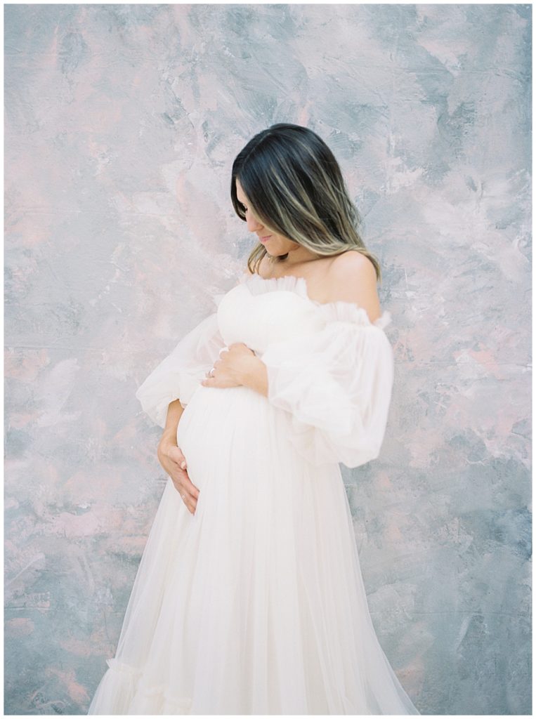 Pregnant mother stands with her hands on her belly during her maternity session in a DC photography studio