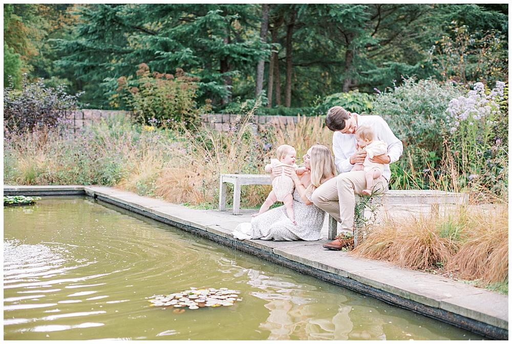 Mother, father, and twin baby girls sit by a pond