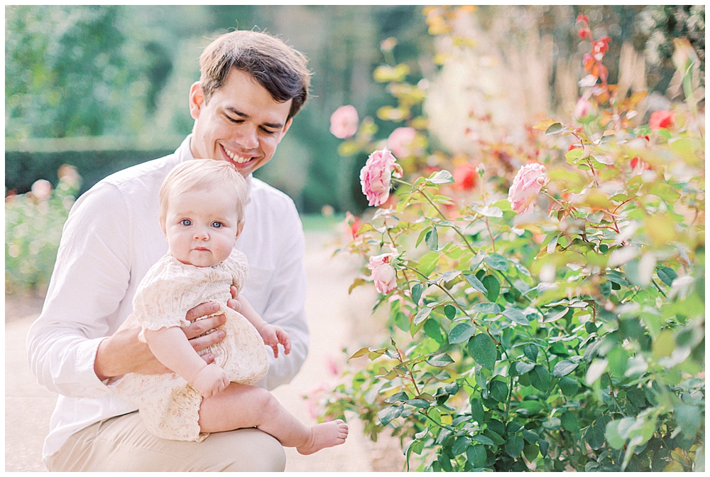Father holds his baby up to roses in a garden