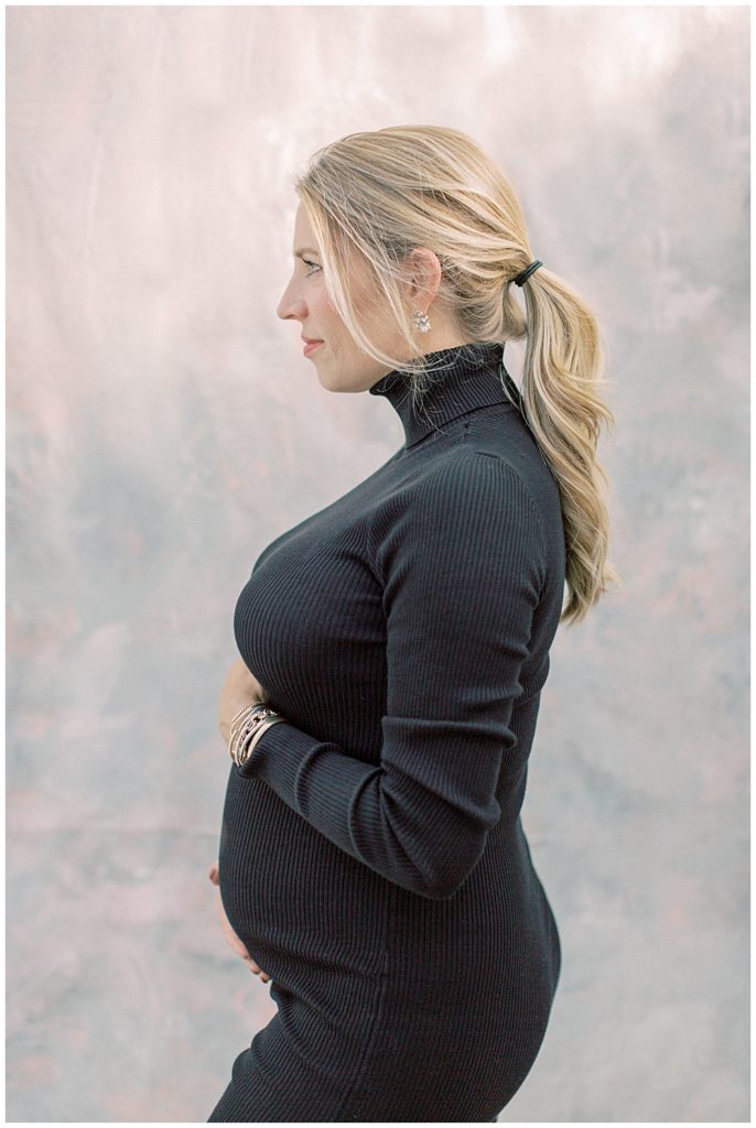Mother stands with one hand on pregnant belly and one hand below