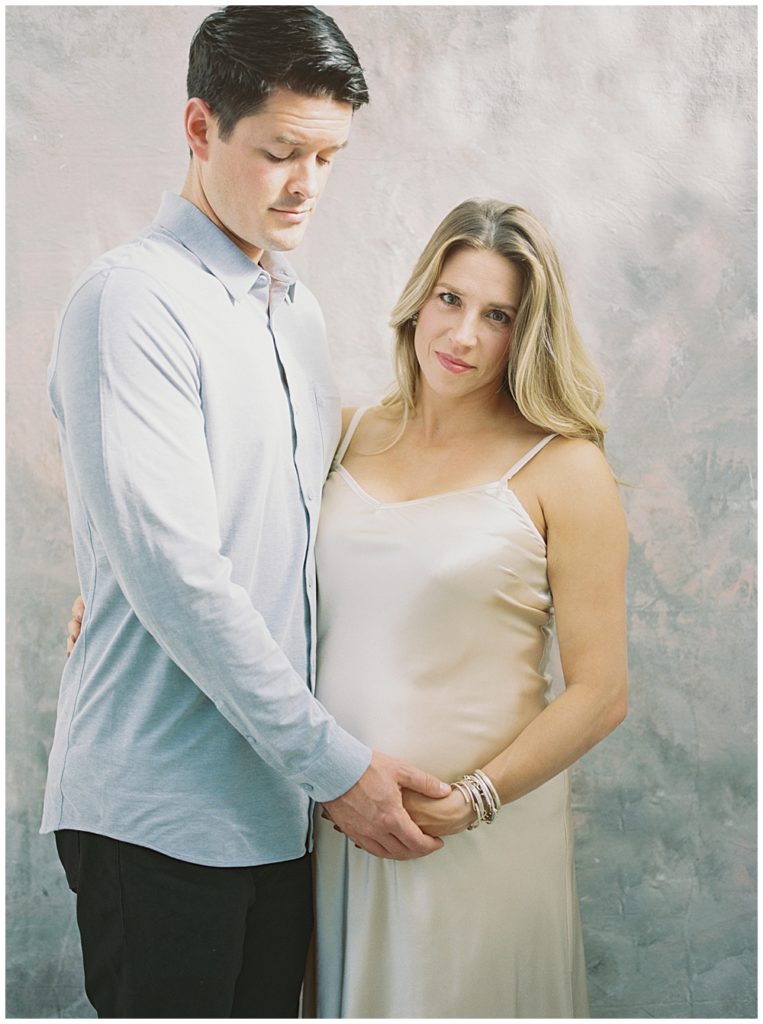Mother and father embrace and touch expecting mother's belly during their Northern VA studio maternity session