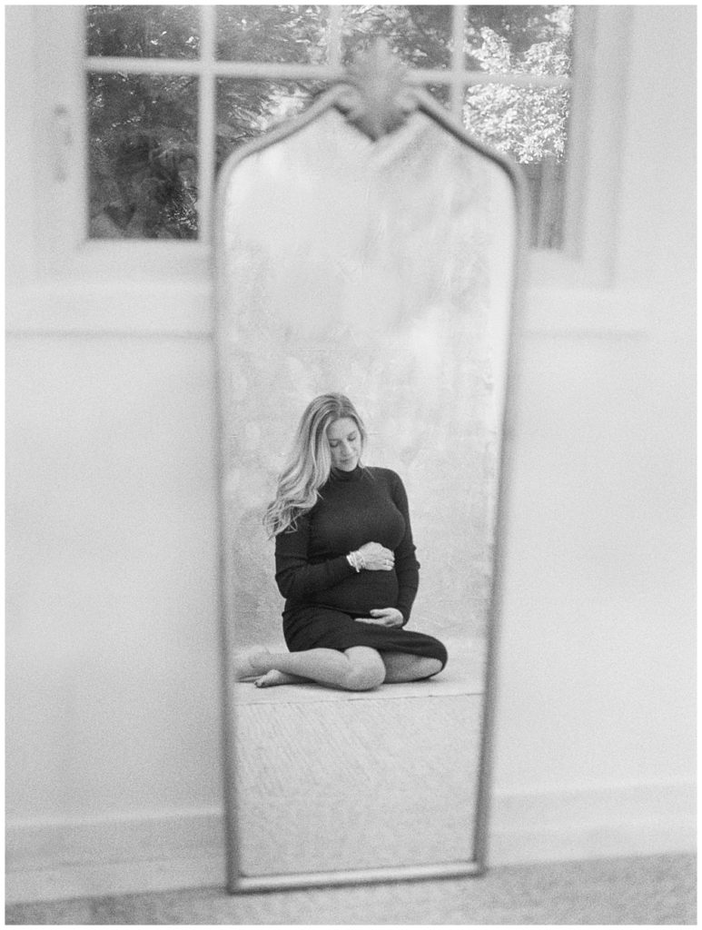 Black and white image of mother sitting in front of mirror during maternity session outside of Northern VA