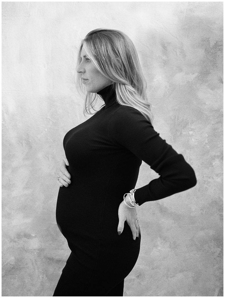 Maternity session where mother stands with one hand on back and one on her belly