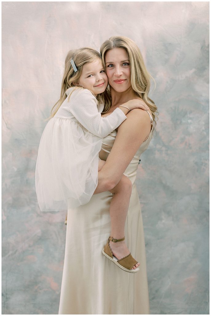 Expecting mother holds her young daughter in an embrace during their studio maternity session