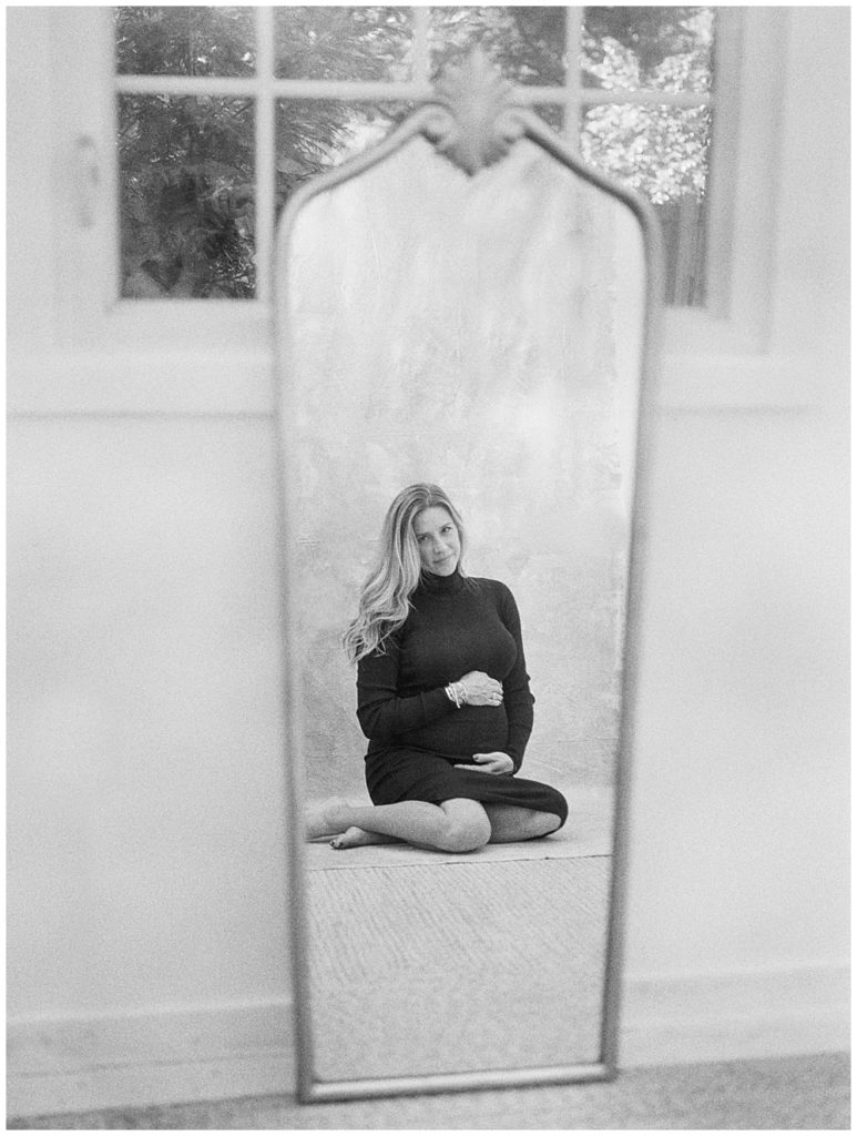 Black and white image of pregnant mother sitting reflected in mirror