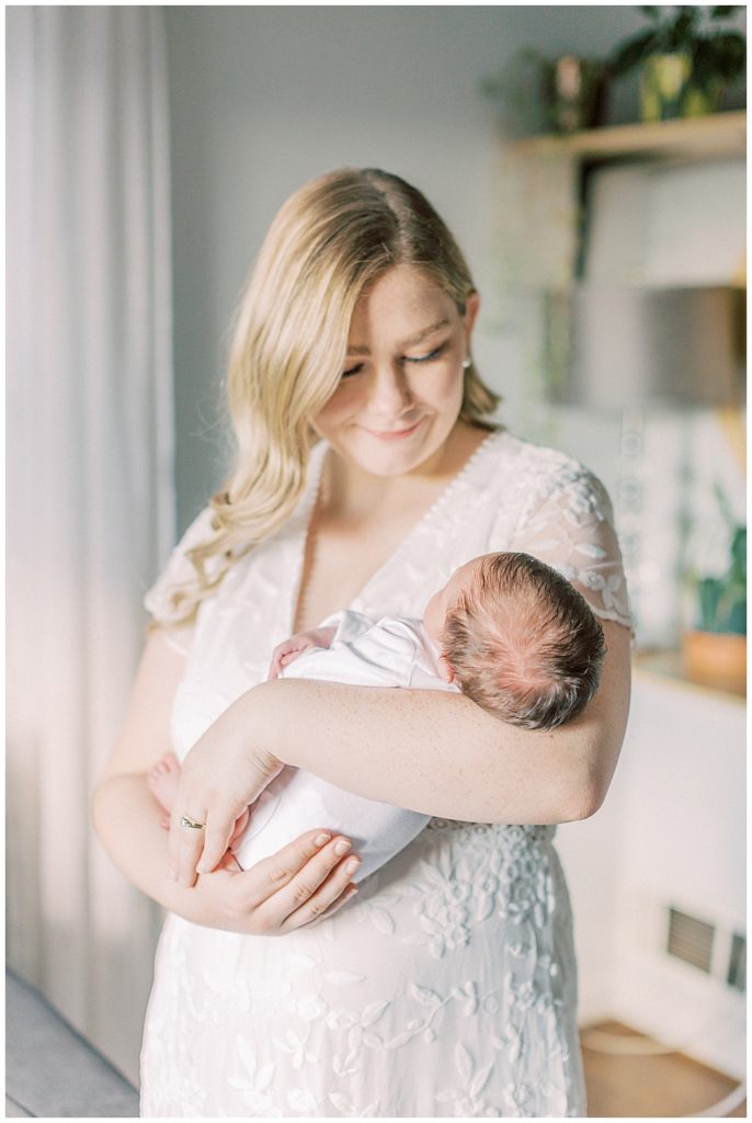 A blonde mother holds her newborn daughter while looking lovingly at her