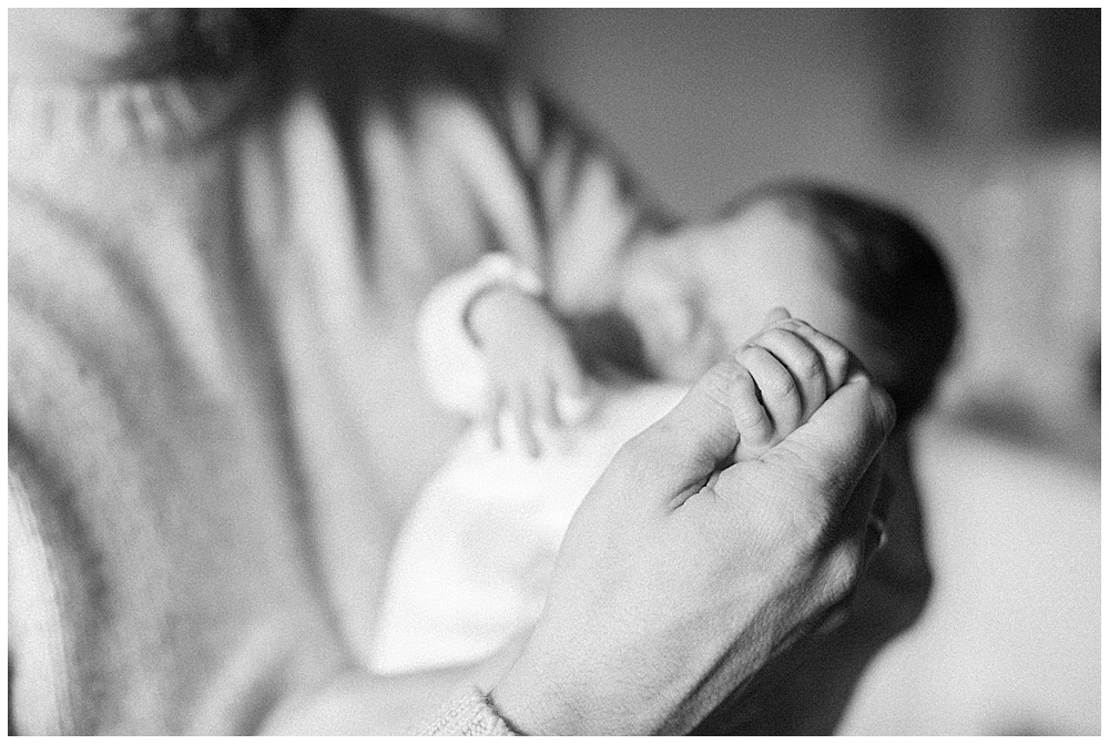 A black and white image of a father holding his newborn daughter's hand
