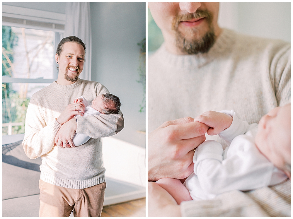 A dad smiles while holding his newborn daughter's hand