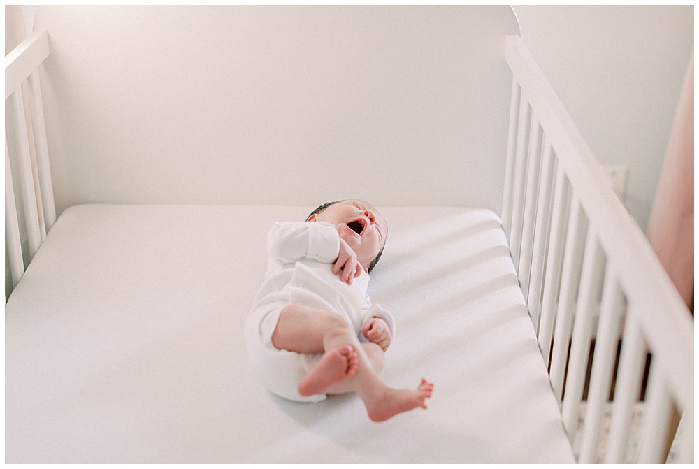 A baby lays in a crib and yawns